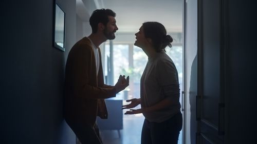 Young Couple Arguing and Fighting. Domestic Violence and Emotional abuse Scene, Stressed Woman and aggressive Man Screaming at Each other in the Dark Hallway of Apartment. Dramatic Scene